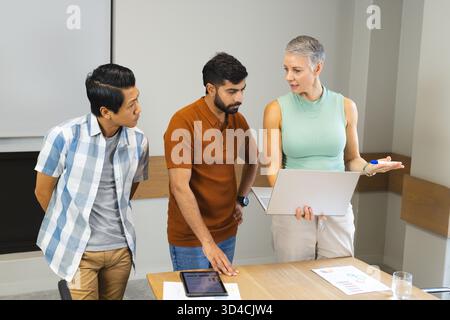Verschiedene Kollegen diskutieren und überprüfen Karten auf einem Laptop in modernen Besprechungsräumen mit Tablet Stockfoto