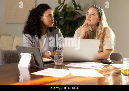 Mit Laptop und Tablet können Sie verschiedene Freundinnen eingeben, die am Tisch im Home Office zusammenarbeiten Stockfoto