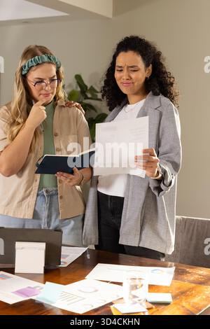 Verschiedene weibliche Kollegen, die Karten am Tisch im Büro studieren, mit blauem Notizbuch und Laptop Stockfoto