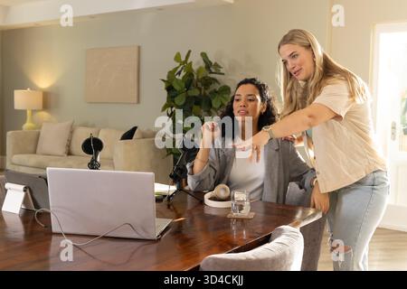 Zusammenarbeit mit verschiedenen weiblichen Kollegen, die Podcasts am Wohnzimmertisch mit Mikrofonen aufzeichnen Stockfoto