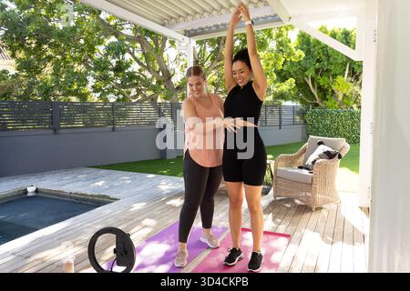Wir führen verschiedene Trainer und Kunden, die sich an Deck am Pool ausstrecken, mit Yogamatten und Ringlicht Stockfoto