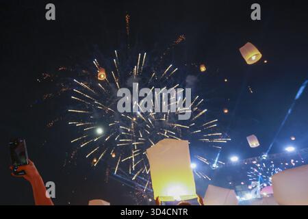 Magische Nachtfestfeier mit hellem Feuerwerk und leuchtender Himmelslaterne. Fröhliche Menschenmenge beobachtet, wie das schwebende Papierlicht den dunklen Himmel erleuchtet Stockfoto