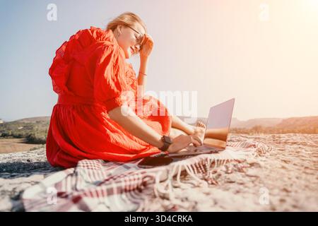 Frau in rotem Kleid, die draußen am Laptop arbeitet Stockfoto