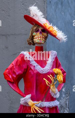 Eine Frau in einem roten Kleid mit einer Blume in der Hand. Die Frau trägt ein Skelett-Kostüm. Mexikanischer Tag der Toten Tradition, Opfer, Essen, Colo Stockfoto