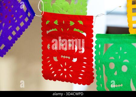Eine rote und grüne Papierlaterne mit einem Schädel hängt an einer Wand. Die Laternen sind bunt. Mexikanischer Tag der Toten Tradition, Opfer, Essen, Farbe Stockfoto