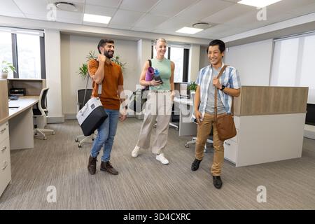 Verschiedene Kollegen gehen in ein modernes Großraumbüro, tragen Sporttaschen und eine gerollte Yogamatte Stockfoto