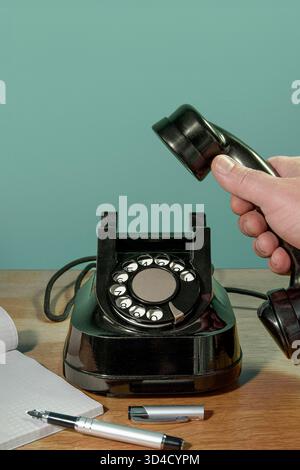 Retro-Telefon, Hand mit Notebook und Stift den Telefonhörer auf dem Schreibtisch abheben. Vertikales Banner auf Grün Stockfoto