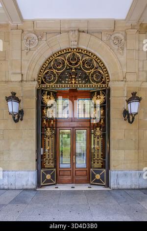 Verzierte goldene schmiedeeiserne Tür mit Bogen und klassischer Steinfassade, detaillierter Eingang des historischen Gebäudes, architektonische Dekoration, elegantes Design Stockfoto
