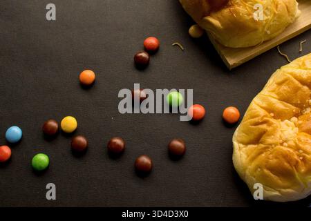Ein Blick von oben bietet eine Auswahl an lebhaften, runden Schokoladenbonbons, die zusammen mit frisch gebackenen Süßkäsebrötchen verstreut sind. Perfekt zum Essen, s Stockfoto