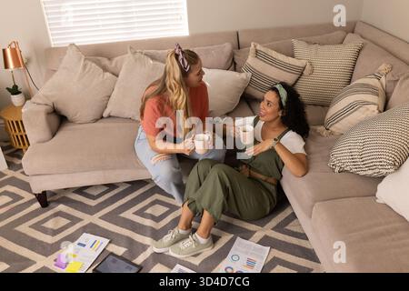 Mit dem Tablet können Sie verschiedene Freundinnen chatten, Karten lesen und aus Tassen im Wohnzimmer schlürfen Stockfoto