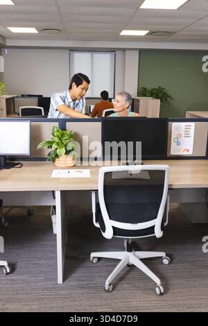 Besprechung der Arbeit verschiedene Kollegen, die sich in modernen Büros über die Trennwand beugen, mit Monitoren Stockfoto