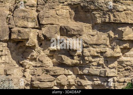Helles Sonnenlicht hebt die zerklüfteten Strukturen einer Felsformation hervor, die Sedimentschichten und natürliche Farbtöne in einer Umgebung im Freien, umgeben von l Stockfoto