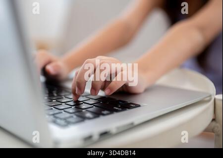 Nahaufnahme eines Paares Kinderhände, die auf einem weißen Tisch auf einem Laptop tippen, während sie auf dem Sofa sitzen. Daten durchsuchen oder Hausaufgaben machen. Stockfoto
