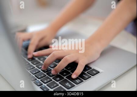 Nahaufnahme eines Paares Kinderhände, die auf der Laptop-Tastatur am weißen Tisch tippen, während sie auf dem Sofa sitzen. Daten durchsuchen oder Hausaufgaben machen. Stockfoto