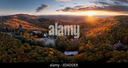 Herbstwald bei Sonnenaufgang mit einem kleinen Dorf in den Bergen Stockfoto