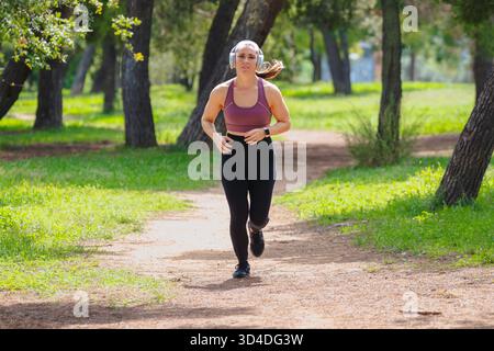 Foto einer Frau, die im Park läuft, Sportkleidung trägt und lächelt Stockfoto