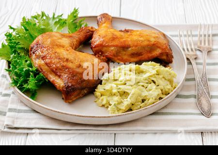 Gebratene Hähnchenschenkel mit Salat und Krautsalat auf einem Teller auf weißem Holztisch mit Gabeln, Serviette, horizontale Ansicht von oben, Nahaufnahme, keine KI generiert Stockfoto