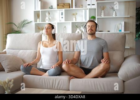 Ein Paar meditiert beim Yoga-Zuhören Online-Guide, der zu Hause auf einer Couch sitzt Stockfoto