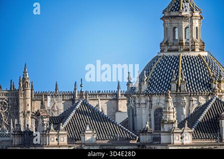 Fangen Sie die atemberaubende blau-weiß gekachelte Kuppel der El Salvador Kirche in Sevilla mit der komplizierten Kathedrale von Sevilla ein, die im Hintergrund steht. Stockfoto