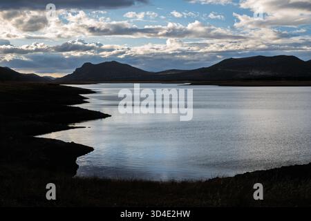 Sanftes Licht reflektiert das stille Wasser des Puente Nuevo Reservoir in der Abenddämmerung, während die Berge der Sierra Morena im Hintergrund verblassen. Stockfoto