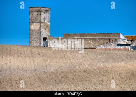 Der Olivenmühlenturm ragt über neu gepflügten Feldern in Huévar del Aljarafe und zeigt seine historischen Wurzeln und mittelalterliche Architektur. Stockfoto
