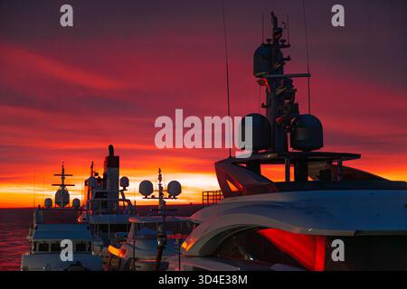 Transport großer Motoryachten über den Ozean bei Sonnenuntergang mit rotem Himmel. Stockfoto