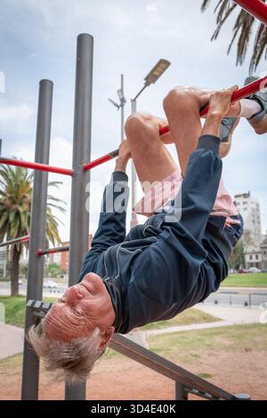 Senior-Mann, der im Freien arbeitet und kopfüber an einer roten Bar hängt Stockfoto