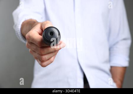 Mann mit versteckter Spionageskamera auf grauem Hintergrund, Nahaufnahme Stockfoto
