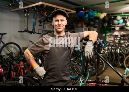 Junger Mann, der in der Fahrradwerkstatt steht und selbstbewusst lächelt Stockfoto
