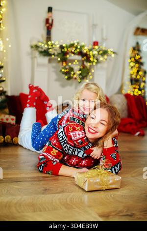Fröhliche Weihnachtsszene mit der Familie, glückliches Kind umarmt Mama, feiert gemeinsam Winterferien drinnen. Stockfoto