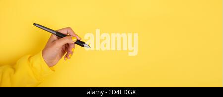 Weibliche Hand, die einen schwarzen Stift vor einem leuchtend gelben Hintergrund hält, ideal für kreative Konzepte, Schreiben und geschäftliche Themen. Stockfoto