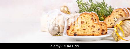 Traditionelles europäisches Weihnachtsgebäck, duftender hausgemachter Stollen, mit Gewürzen und getrockneten Früchten. Geschnitten auf weißem Tisch mit Weihnachtsbaumzweig Stockfoto