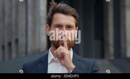 Porträt kaukasischer Geschäftsmann zeigt Stille Geste Schweigen Zeichen reifer Geschäftsmann in der Stadt männlicher Arbeiter Unternehmer mit Finger mear Mund verboten Stockfoto