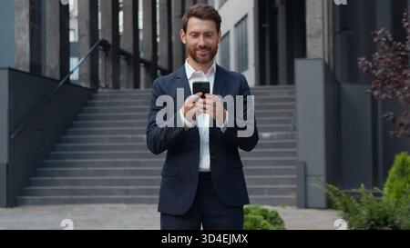 Kaukasischer reifer erfolgreicher Geschäftsmann in der Stadt Geschäftsmann mit Telefon hält Smartphone mit mobiler Anwendung überprüft E-Mail männlicher Erwachsener Stockfoto