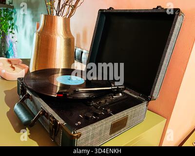 Kiew, Ukraine - 10. November 2025: Retro-Plattenspieler mit Vinyl auf einem texturierten Gehäuse neben einer Vase und einer Kerze in einer warmen Heimszene. Stockfoto