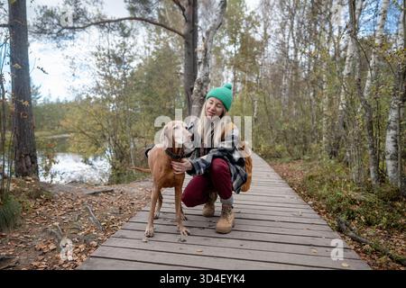 Wanderer auf täglichem Spaziergang im Herbstwald zusammen mit Hund, sitzend auf einem Holzweg in der Nähe des Sees. Stockfoto