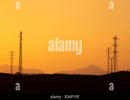 Calima, Sandsturm auf Lanzarote. Blick auf Vulkane und Stromübertragungsmasten in der Silhouette vor orangem Himmel. Costa Teguise, Kanarische Inseln. Stockfoto