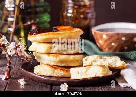 Fastenpfannkuchen mit Pflaumenmarmelade und Tee und ein Strauß blühender Aprikosenzweige auf einem Holztisch. Rustikaler Stil, selektiver Fokus. Stockfoto