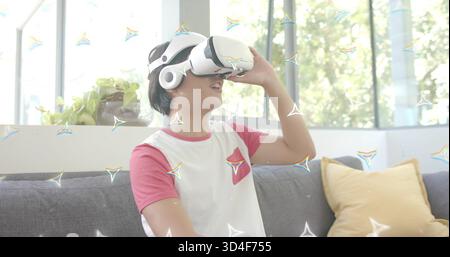 Anpassender asiatischer Mann mit weißem VR-Headset, rotem Raglan-T-Shirt in der hellen Lounge und Senfkissen Stockfoto