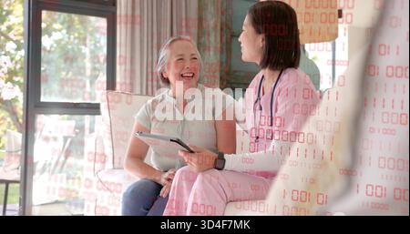 Sitzende Krankenschwester in rosafarbenen Strümpfen, die sich auf dem Sofa des Wohnzimmers zum Senioren neigen, Tablette, Stethoskop zeigt Stockfoto