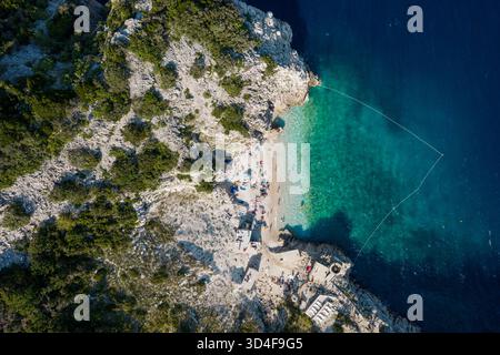 Blick aus der Vogelperspektive auf türkisfarbenes Wasser, zerklüftete Klippen und einen sonnendurchfluteten Strand voller Leben, Brsec, Istrien, Kroatien. Stockfoto