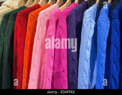 Warme Strickpullover, die ordentlich auf Kleiderbügeln angeordnet sind. Stockfoto