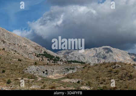 Das römische Theater Sagalassos befindet sich am Fuße der steilen Berge mit dramatischen dunklen Wolken, die darauf herabfallen. Majestätische Natur und Architektur. Stockfoto