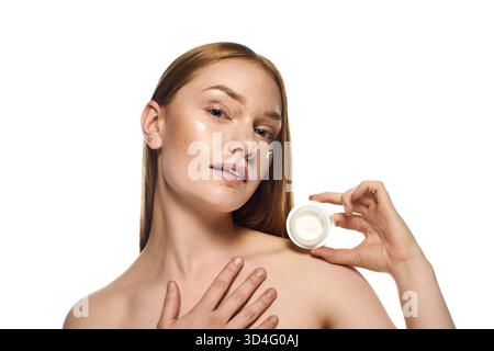 Eine junge Frau zeigt ihre strahlende Haut, während sie ein Hautpflegeprodukt mit einem ruhigen Ausdruck aufträgt. Stockfoto