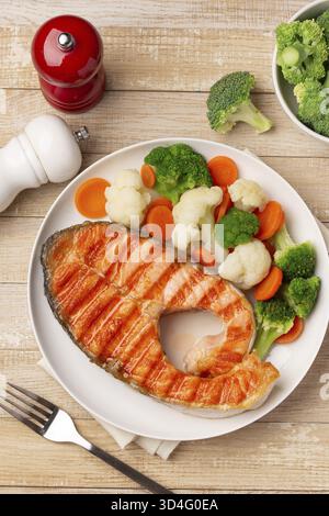 Speisen, gegrillter Lachs und Gemüse auf weißem Teller, hölzerner Hintergrund, Blick von oben Stockfoto