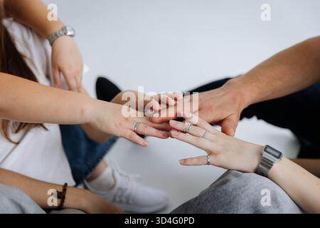 Junge Freunde, die Hände stapeln, zeigen Einheit und Unterstützung auf hellem Hintergrund Stockfoto