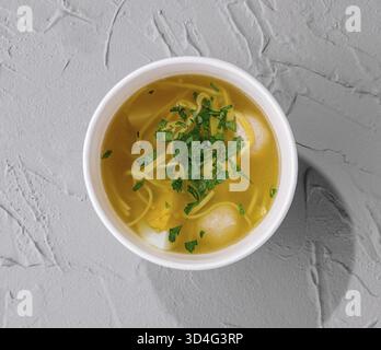 Essen, Blick von oben auf eine gemütliche Schüssel mit Hühnchennudelsuppe garniert mit Petersilie auf einer strukturierten Oberfläche Stockfoto