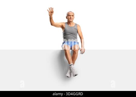 Älterer Mann in Sportbekleidung, der auf einer leeren Platte sitzt und isoliert auf weißem Hintergrund winkt Stockfoto