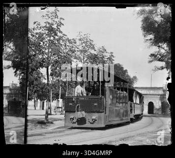 Ein Zug mit seinem Ingenieur auf einem von Bäumen umgebenen Platz, fotografiert von Antoni Bartumeus i. Casanovas zwischen 1897 und 1925. Das Bild zeigt den Transport aus dem frühen 20. Jahrhundert in einer urbanen Umgebung. Stockfoto