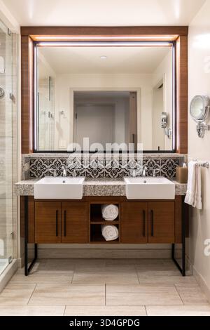 Ein Badezimmer mit Holzschrank und gerahmtem Spiegel, Schürzwaschbecken mit Chromarmaturen, Fliesenplättchen und Keramikfußboden. Stockfoto